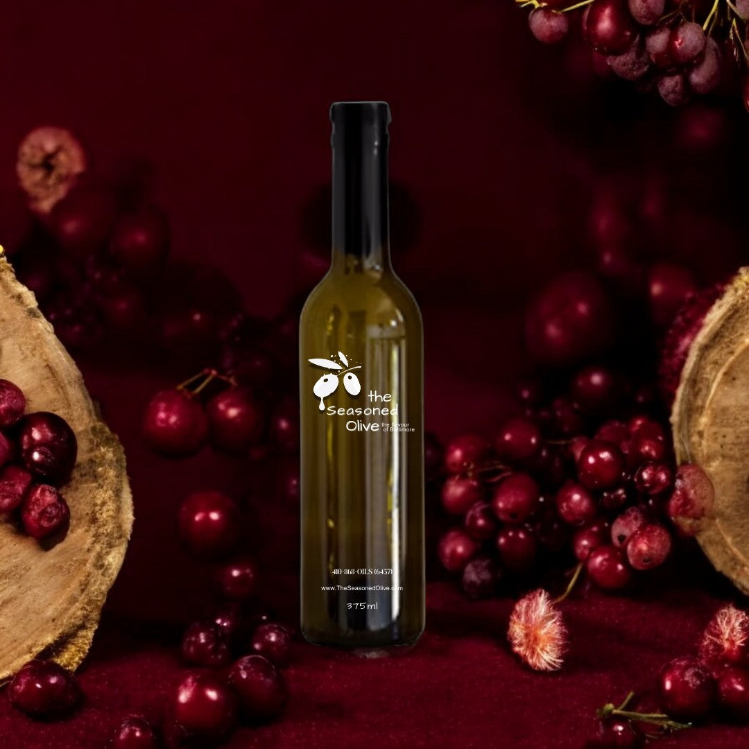 Bottle of Cabernet Sauvignon Vinegar set against a deep burgundy background with wine barrels and dark grapes in the background, highlighting its full-bodied and rich flavor. Subtle hints of cranberries and beef stock suggest its perfect use in marinades and reductions.